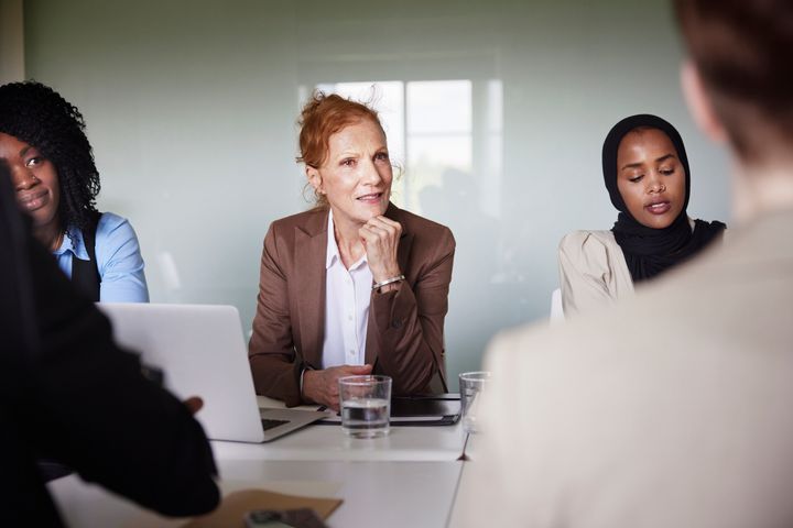 En kvinnlig chef omgiven av flera kollegor sitter vid ett bord i ett konferensrum.
