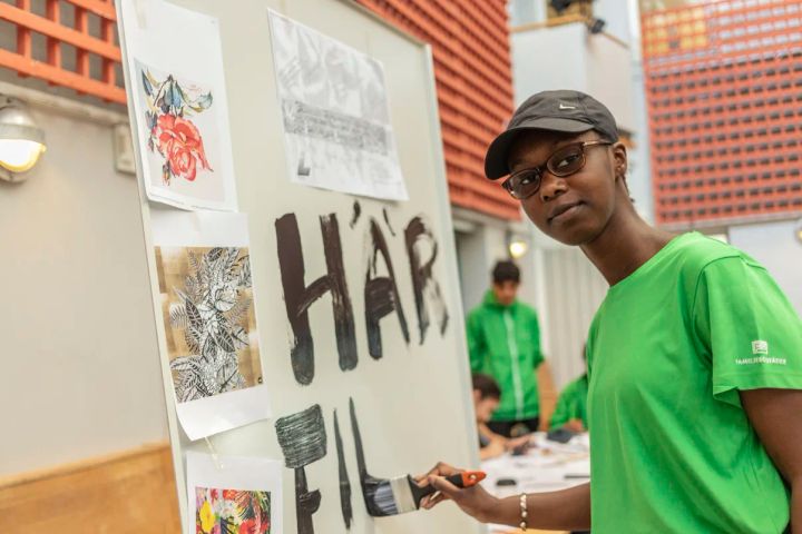 Nio ungdomar har som sommarjobb att måla ett konstverk på byggplanket runt det nya polishuset i Rinkeby. Här provar Fatou Njie olika designidéer. Foto: Niklas Palmklint