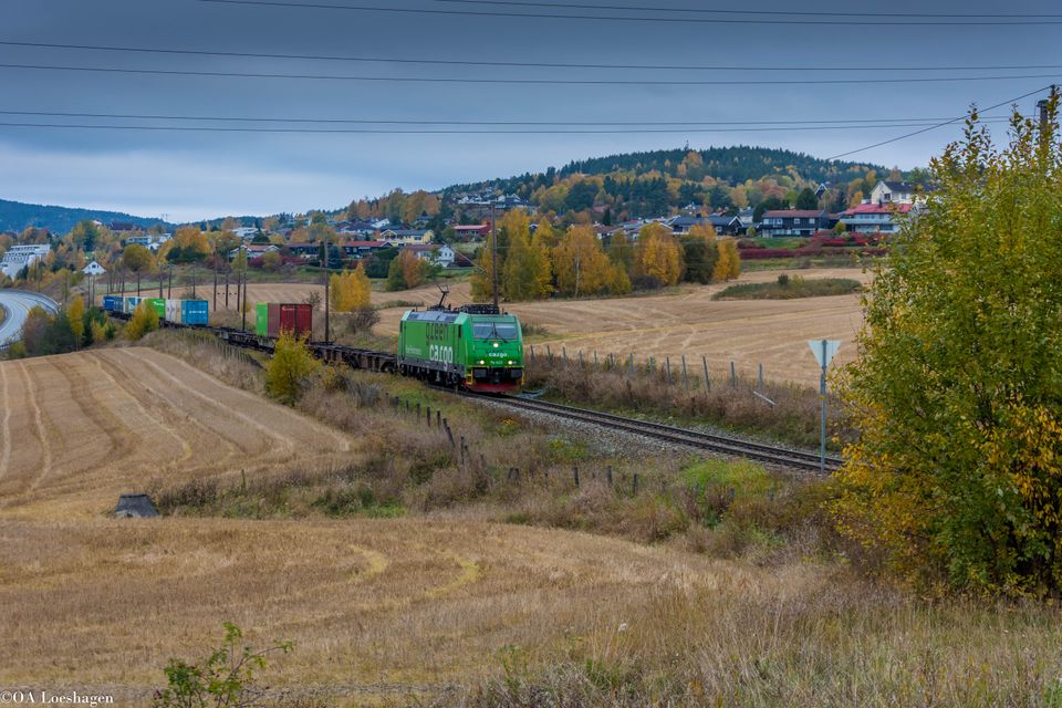 Green Cargos godståg passerar samhälle och åkrar en höstdag