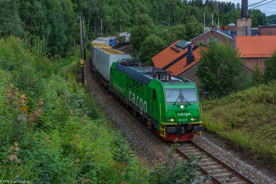 Green Cargos godståg passerar samhälle och vacker natur på sommaren.