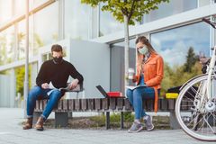 Syntolkning: Två studenter med munskydd sitter utanför en universitetsbyggnad.