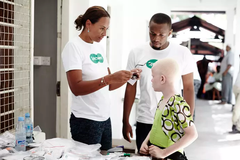 Specsavers Ge Syn Lotta Gray med flicka Albinos är utsatta på flera sätt i Tanzania. De är oerhört ljuskänsliga och denna elvaåriga flickas ögon hade blivit exponerade för ljuset så mycket att hon hade grava synfel och endast såg ljus och mörker och konturer. Hon hade även muskelryckningar i ögonen och det fanns inga optiska glasögon som kunde hjälpa henne. Med solglasögon lindrades huvudvärk och obehag.