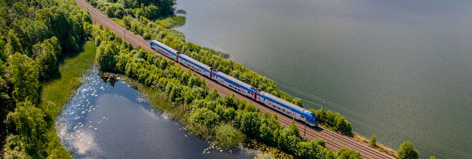 Mälartågs dubbeldäckare passerar genom ett naturskönt Mälardalen.