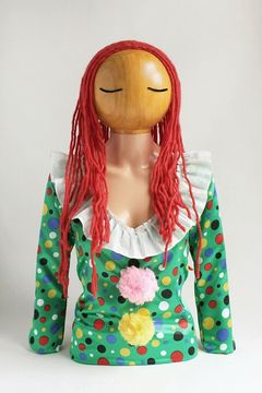 Överdel av docka med huvud i trä, ögonen är markerde med streck, håret är av rött garn.  Dockan är klädd i prickig dress.