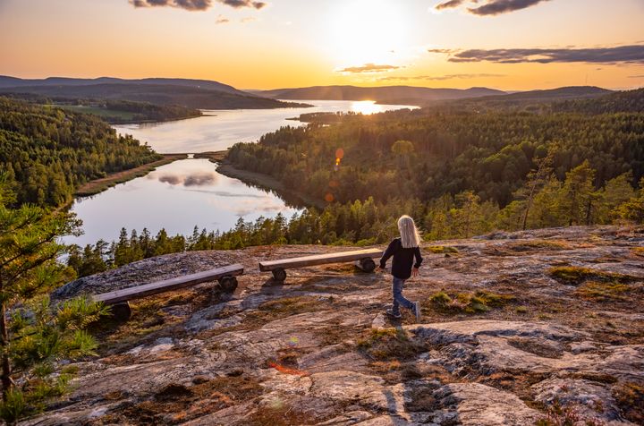 Liten flicka står på berghäll i Höga kusten och blickar ut över kvällsljus i kustbandet
