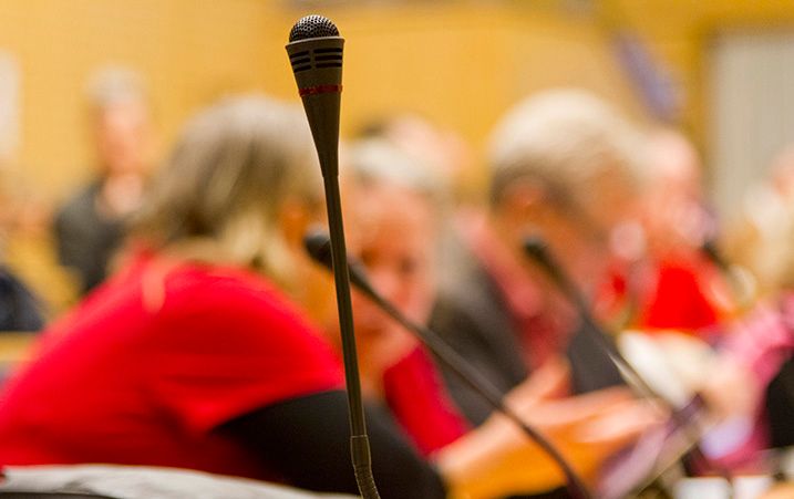 I förgrunden en mikrofon, i disad bakgrund mötesdeltagare