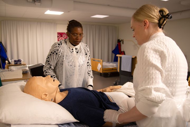 Två vårdanställda står vid en säng där en patientdocka ligger nerbäddad.