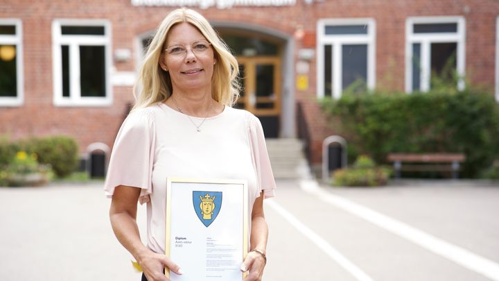 Glad rektor visar upp diplom på skolgård framför Blackebergs gymnasieskola