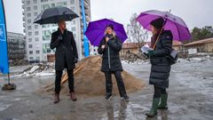 Tre personer med paraplyn framför en grushög, foto.