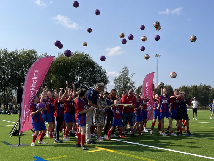 Bandklippning på fotbollsplan och många barn som slänger upp fotbollar i luften