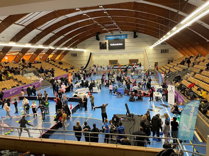 Bild på idrottshall full med människor och aktiviteter vid olika montrar