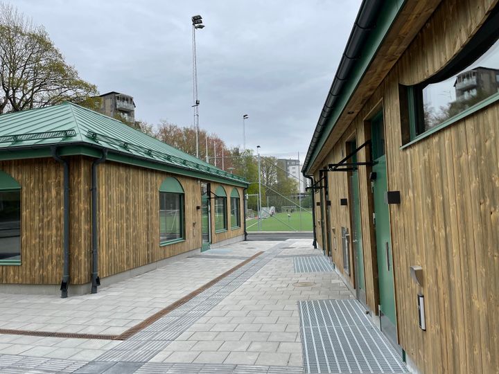 Två träfärgade byggnader och i bakgrunden skymtar en fotbollsplan