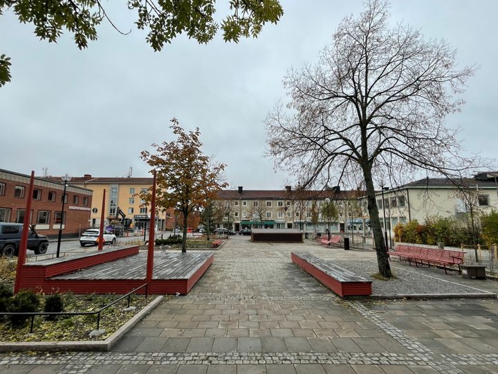 Torg med scen till vänster och flera träd.