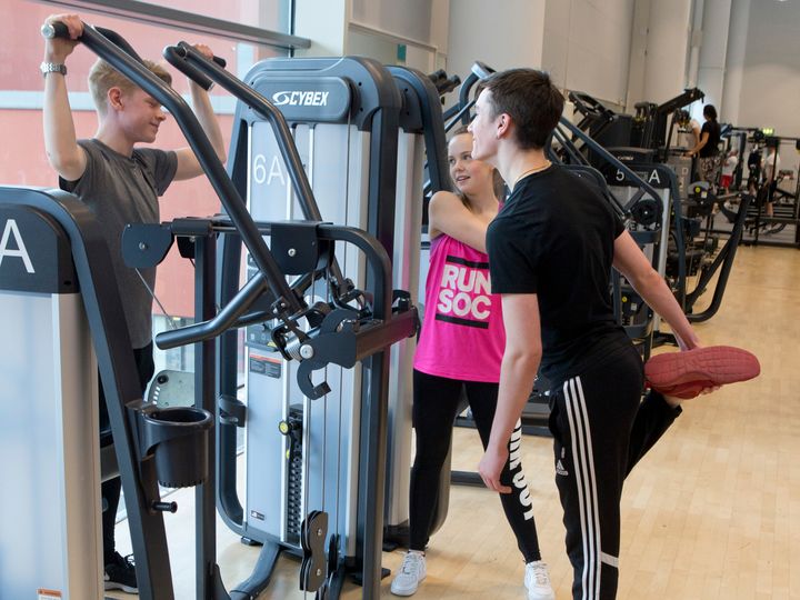 Tre ungdomar vid en maskin i ett gym