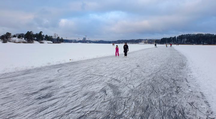 En sjö med plogad bana och skridskoåkare i bakgrunden