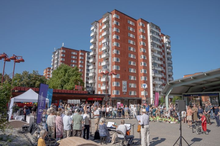 Människor på ett torg. Högt hus i baggrunden.