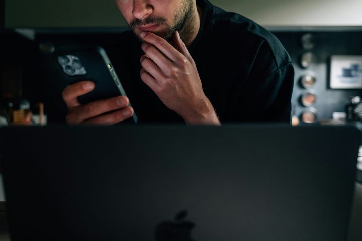 Person sitter vid en dator och tittar samtidigt på en smartphone