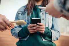 Ung person står och håller i en mobiltelefon. Fler unga, också med mobil, står runt omkring.