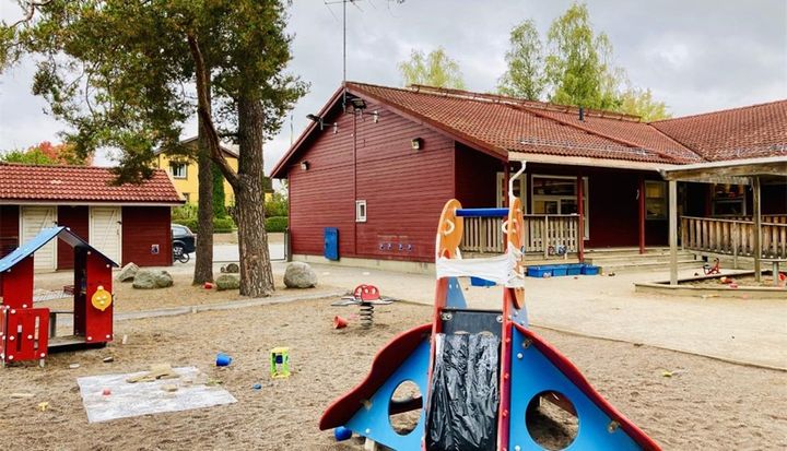 Röd förskolebyggnad i ett plan med gårdsyta framför.