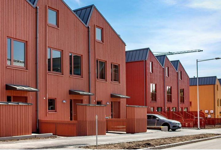 Röda radhus längs en gata. En bil står parkerad framför ett av husen.