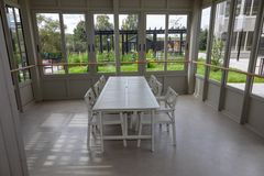 Ett inglasat rum med ett vitt matbord och åtta stolar. Utsikt över en grönskande trädgård utanför.