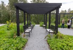 Pergola med bänkar längs en grusväg omgivet av grönska.