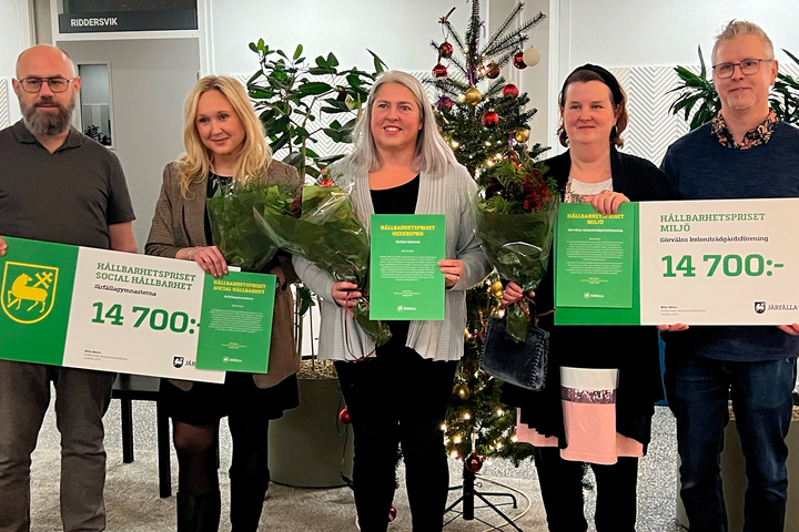 Fem personer står framför gröna växter och håller upp stora prischeckar och diplom.