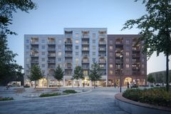 En modern byggnad med kommersiella lokaler på bottenplan, omgiven av ett torg med träd och gångvägar.