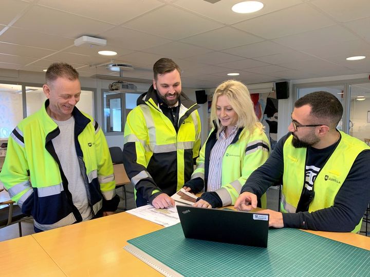 Fyra personer i arbetskläder tittar på planer i ett kontorsrum.