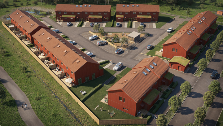 Flygfoto av ett bostadsområde med röda radhus runt en gård med bilparkeringar och grönområden.