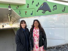 Två personer står framför en vägg med fågelmålning och musiknoter.