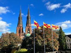 Svenska kyrkans flaggor vajar framför Uppsala domkyrka under en klarblå himmel.