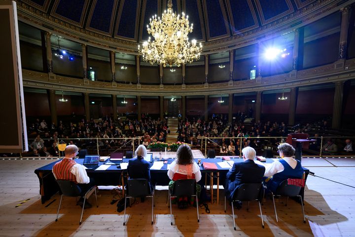 Bild av Kyrkomötets presidium som leder första sessionen i Uppsala universitets aula, stor ljuskrona ovanför.