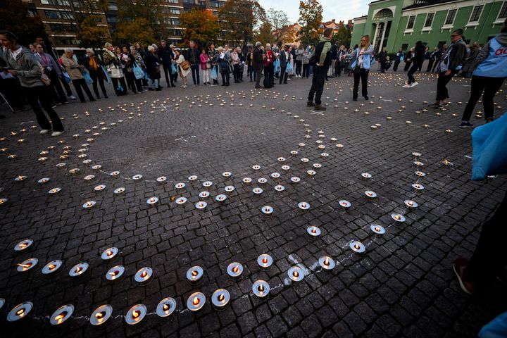 En grupp människor står kring ett spiralformat ljusarrangemang på marken under en utomhusceremoni.