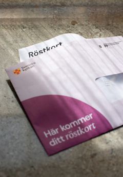 Ett röstkort sticker ut från ett öppnat kuvert som ligger på ett bord.