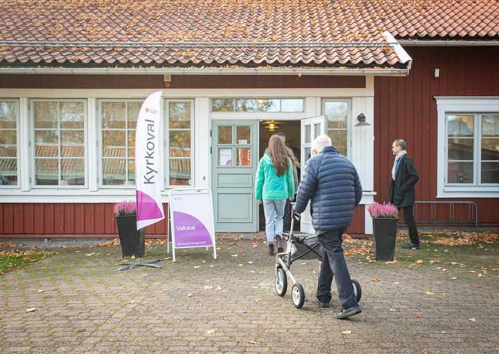 Personer går in i en byggnad med en skylt som säger "Kyrkoval".