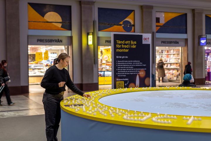 En person tänder digitala ljus vid en rund installation på Stockholms Centralstation, arrangerad av Act Svenska kyrkan som en del av en ljusmanifestation för fred.