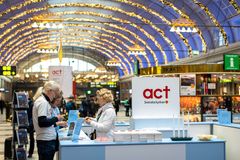 Tre personer vid en informationsdisk för Act Svenska kyrkan på en juldekorerad tågstation.
