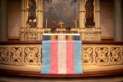 En kyrka dekorerad med taxtilier i regnbågsfärger och en transflagga.