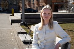 Kvinna i vårsolen på en parkbänk. Hon har ljust långt hår och tittar leende in i kameran.