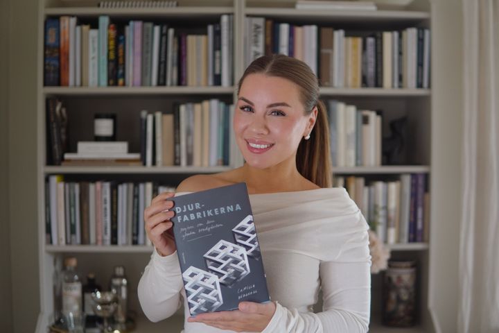 Therese Lindgren håller boken Djurfabrikerna framför en bokhylla.