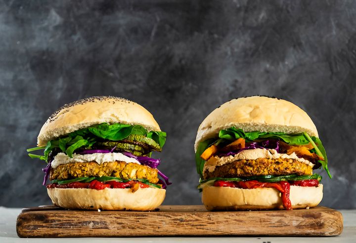 Två vegetariska hamburgare med färgglada grönsaker på ett träunderlag.