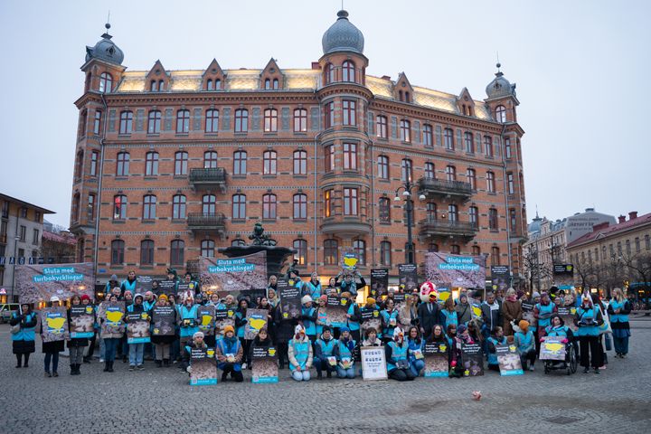 En grupp människor samlade för en demonstration framför en stor, äldre byggnad. De håller i skyltar och banderoller.
