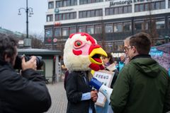 En person med ett stort hönshuvud på huvudet pratar med en annan person utomhus.