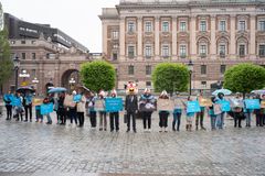 En grupp människor står utanför ett historiskt byggnad, bärande skyltar och paraplyer.