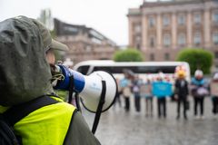 Person i regnrock använder en megafon för att adressera en grupp människor på en gatudemonstration.