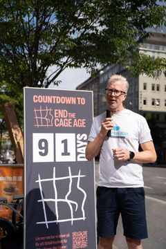 En person talar vid en demonstration framför en skylt där det står "Countdown to end the cage age 91 days".