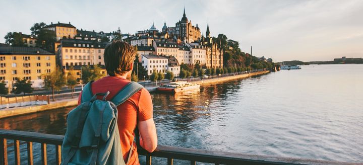 Person med ryggsäck tittar ut över vattnet, en stad i bakgrunden.