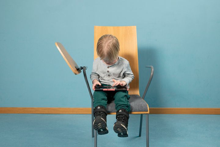 Ett litet barn sitter på en stol och använder en surfplatta.