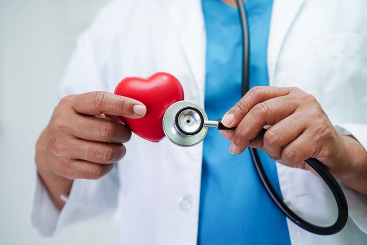 En läkare i vit rock håller ett stetoskop mot ett rött hjärta i plast.